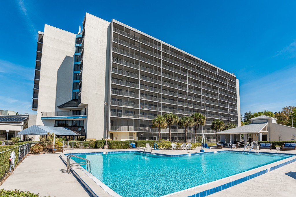A modern hotel with a large outdoor swimming pool under a clear blue sky.