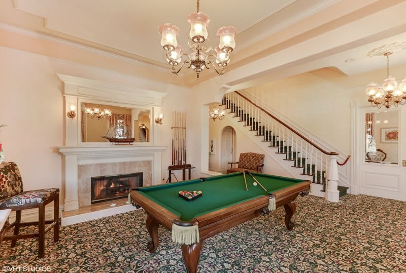 A vintage-style billiard room featuring a pool table, chandelier, and a fireplace.