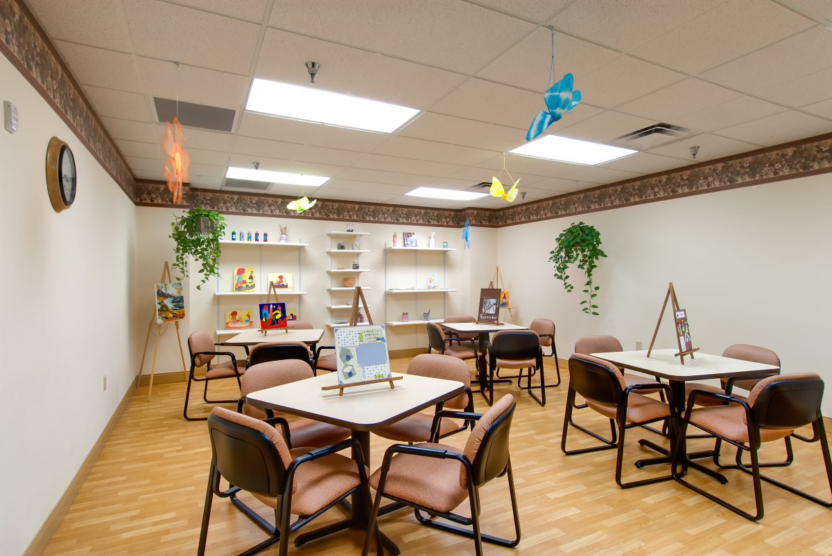A community room with tables, chairs, and bookshelves, decorated with plants and hanging ornaments.