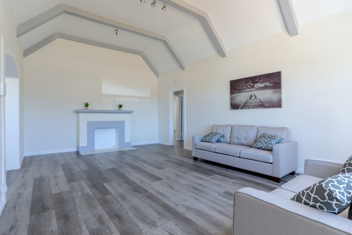 A minimalist living room with a modern design, featuring a sofa, fireplace, artwork, and hardwood flooring.