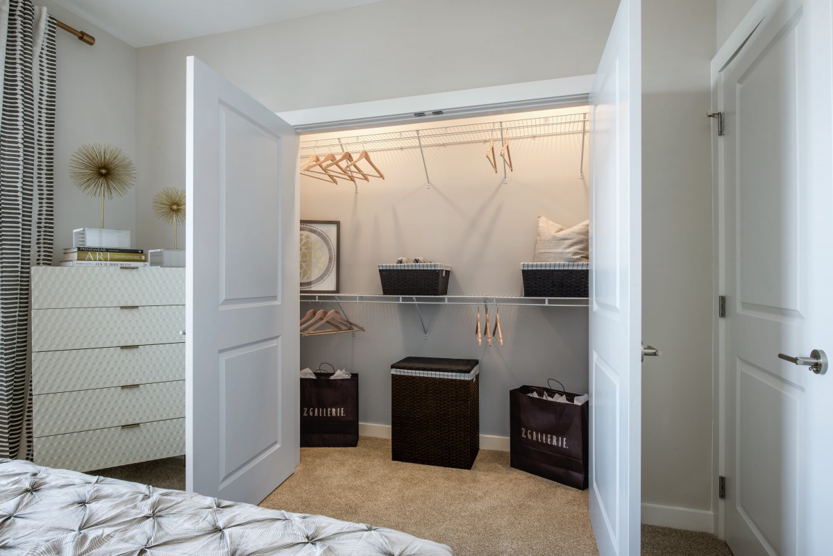An organized bedroom closet with open doors, featuring shelves, hangers, and storage baskets.