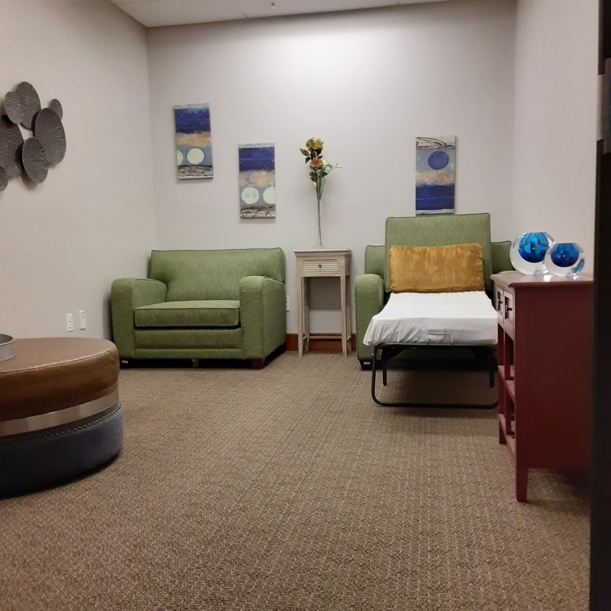 A cozy room with a green chair, sofa, decorative artwork, and a small table with ornaments.