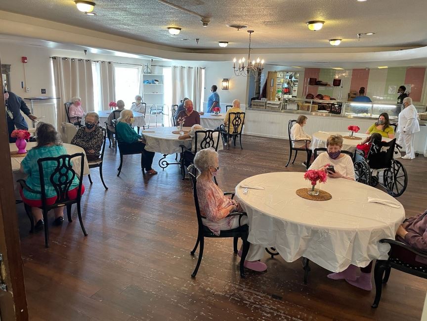 A communal dining area with elderly residents gathered around tables in a senior living facility.