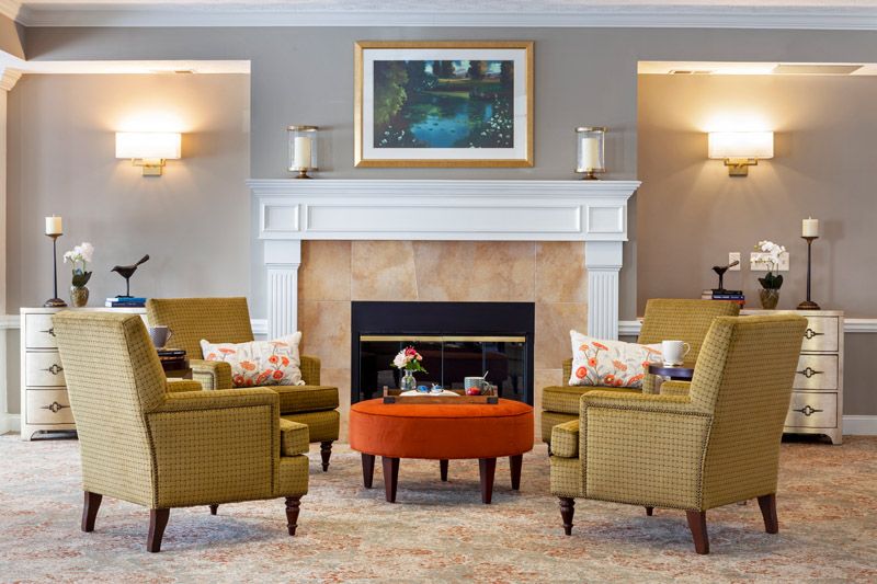 A cozy living room with a central fireplace, surrounded by stylish chairs and an orange ottoman, complemented by wall art.