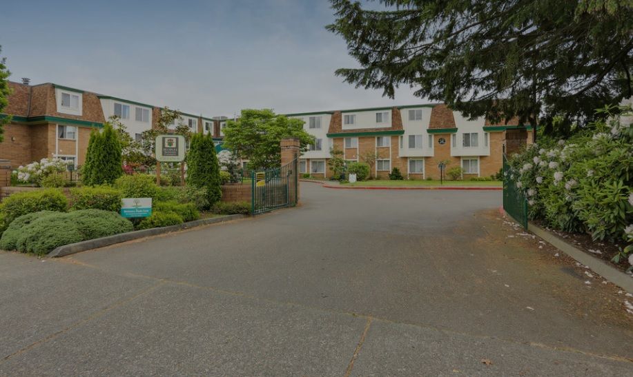 A residential apartment complex with landscaped surroundings and a parking area.