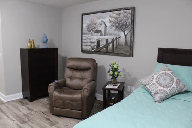 A cozy bedroom featuring a recliner, a bed with teal bedding, and a wall painting.