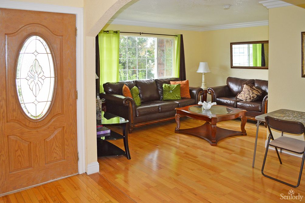 A cozy living room with wooden floors, a leather sofa set, and a large window bringing in natural light.