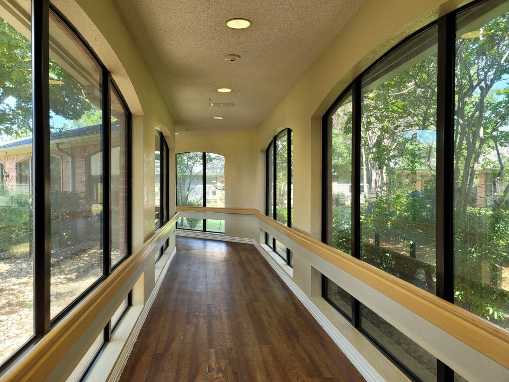 A well-lit corridor with large windows and a wooden floor.