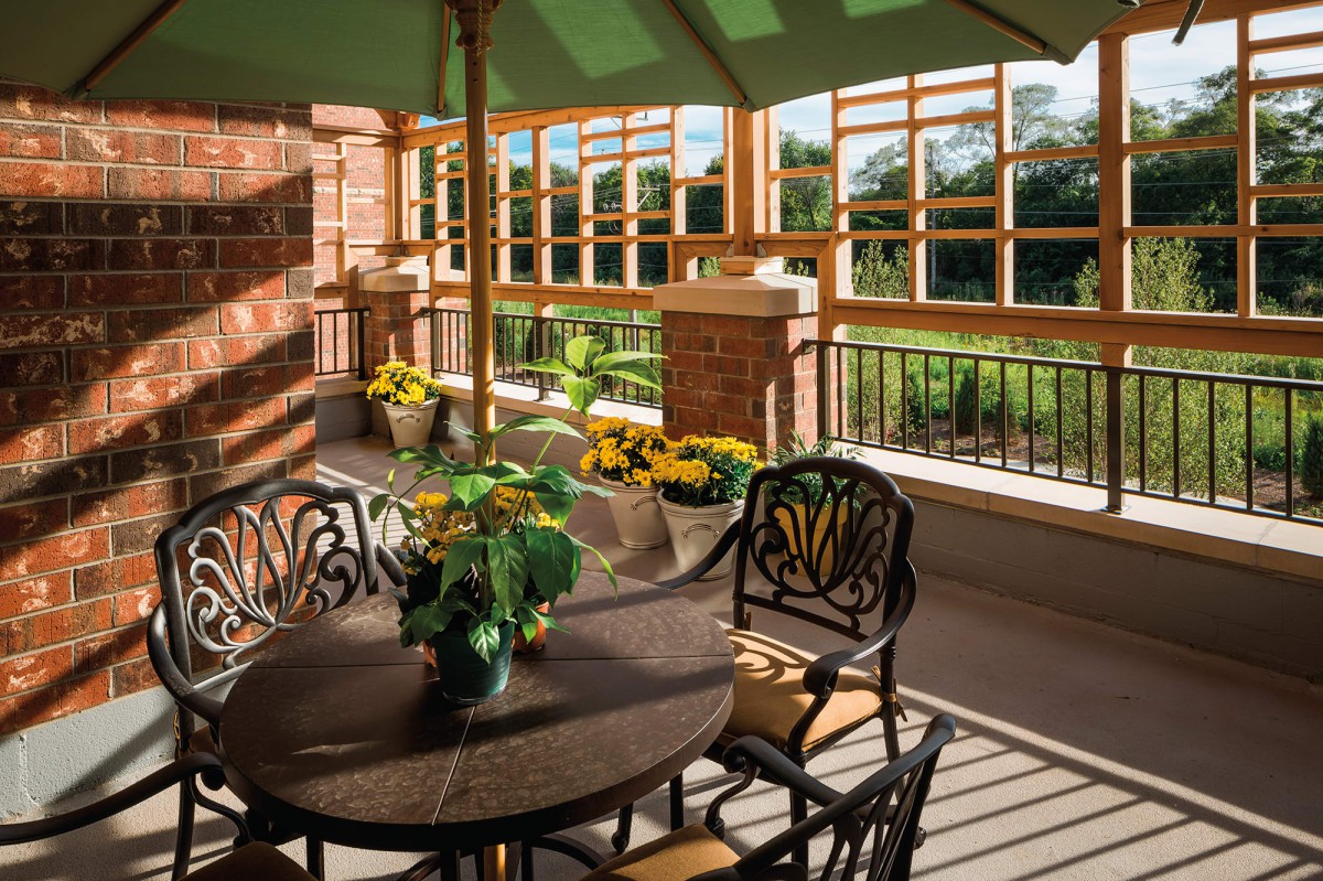 A sunlit patio with elegant furniture and vibrant flowers under a green umbrella.