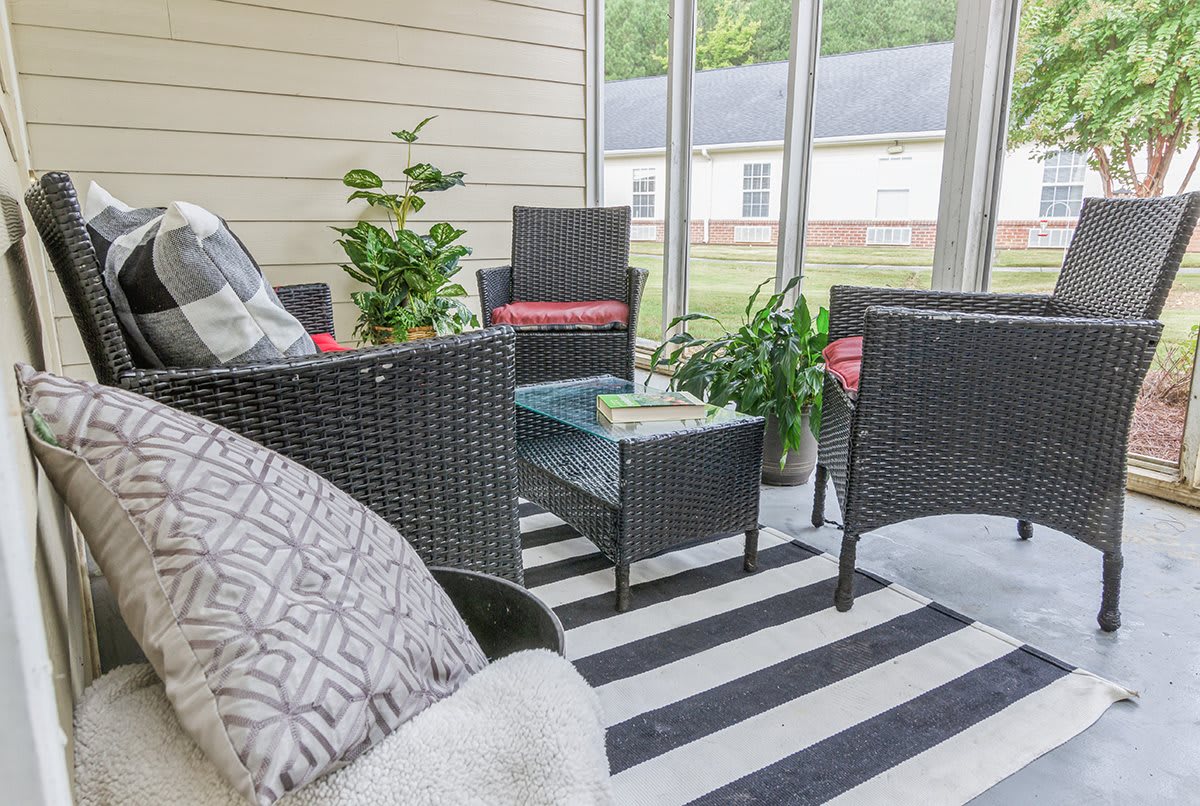 A cozy patio setup with rattan furniture, a striped rug, and lush plants.