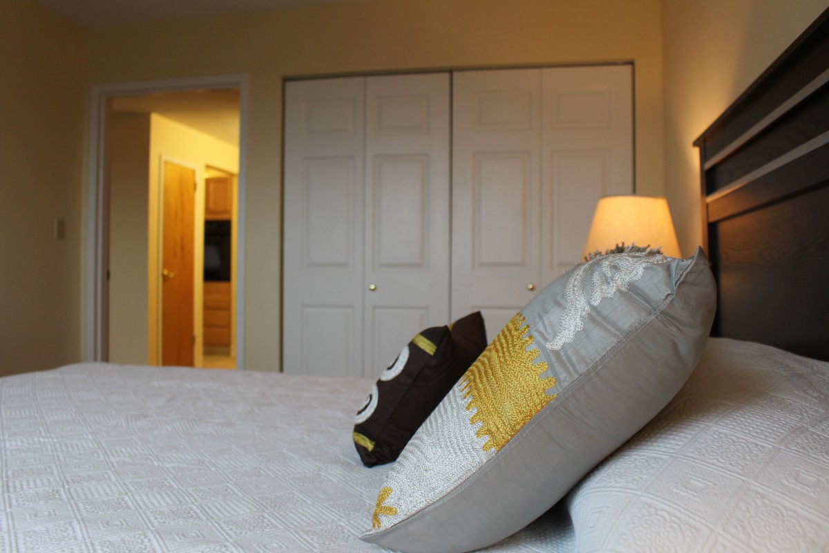 A cozy bedroom with decorative pillows and a warm-lit lamp beside a closet.