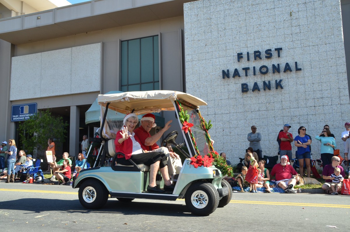 A golf cart decorated for a parade passes by the First National Bank building on a sunny day.