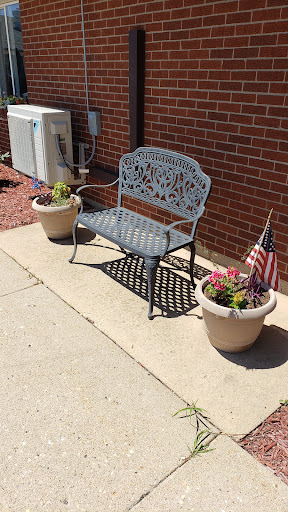 A decorative bench surrounded by potted flowers and an American flag.
