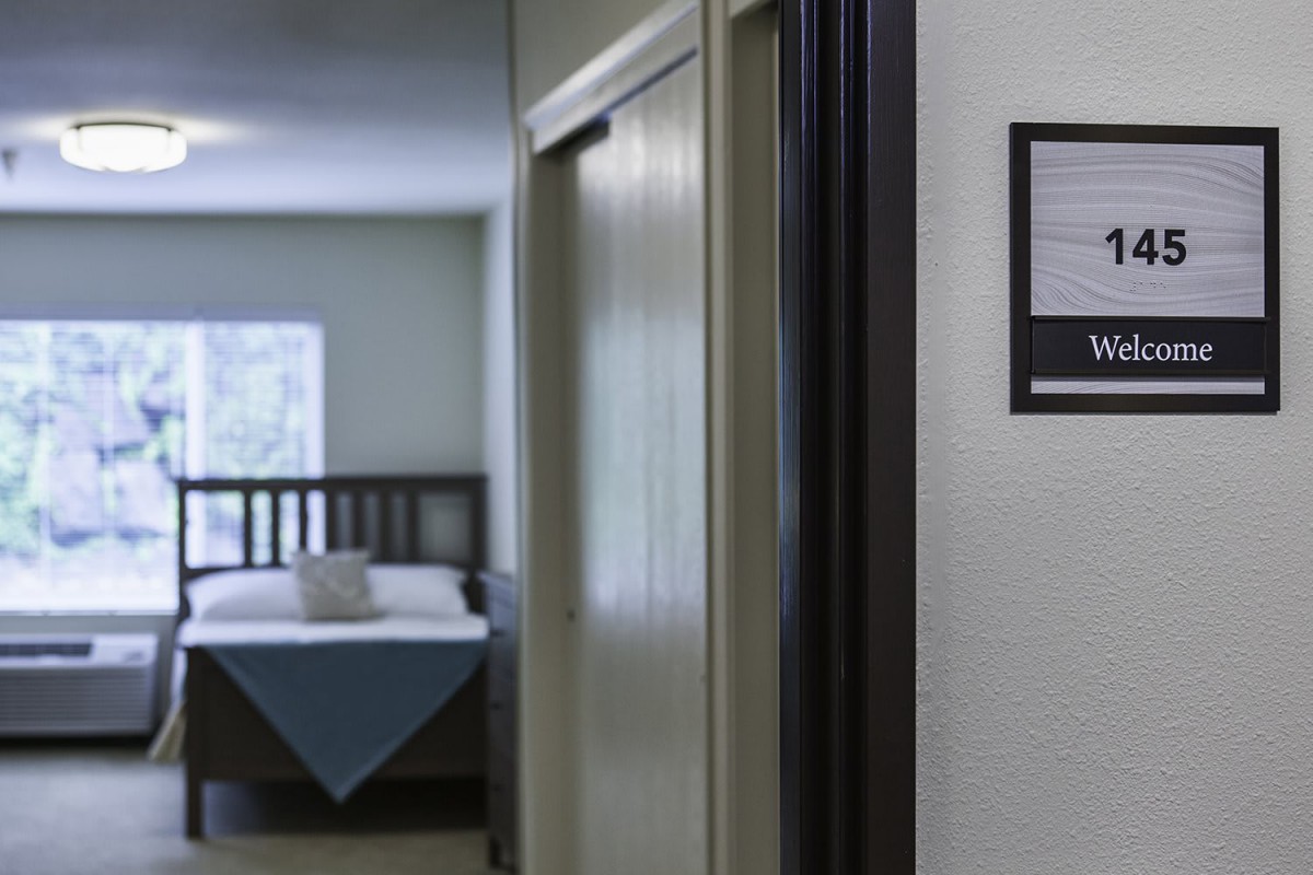 A view into a cozy hotel room through an open doorway, showcasing a bed with neatly arranged pillows.