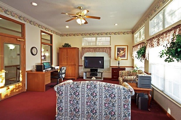 A cozy living room with a television, sofa, desk, computer, and ceiling fan.
