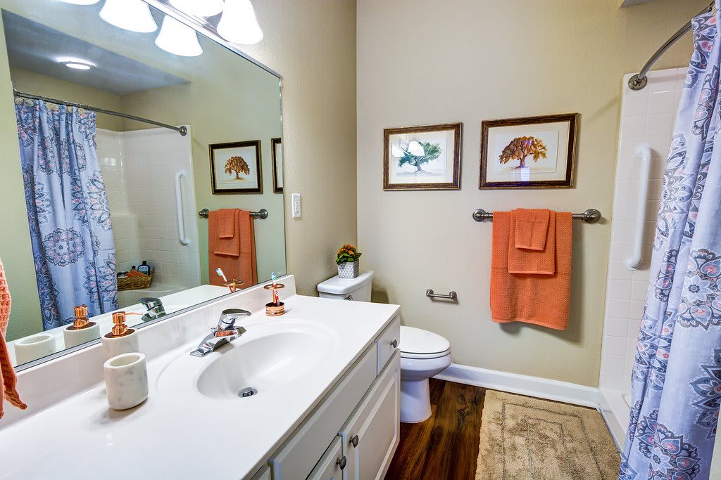 A well-decorated bathroom featuring a mirror, sink, and orange towels with framed artwork on the wall.