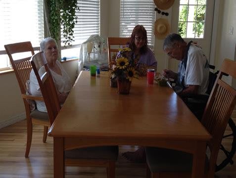 A family gathering around a dining table in a bright room with plants and sunflowers.