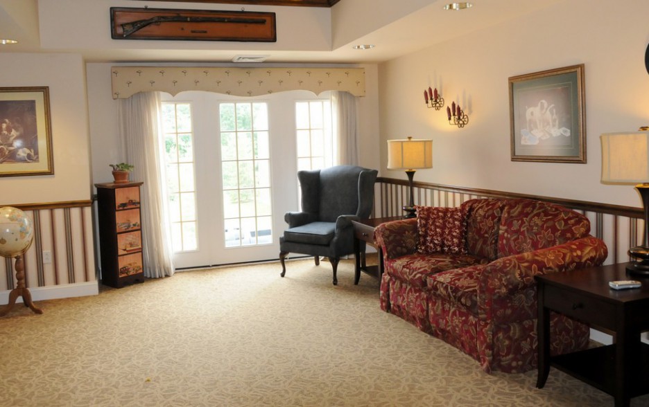 A cozy living room with a floral sofa, armchair, and bright natural light coming through French doors.