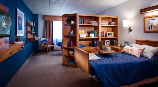 A cozy and organized interior space featuring a desk, shelves, and a neatly made bed.