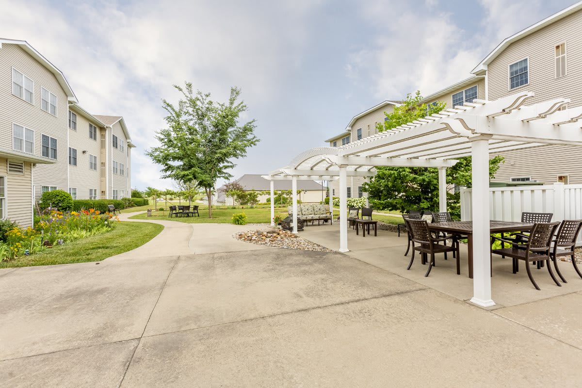 A peaceful outdoor space featuring a pergola with seating, surrounded by greenery and apartment buildings.