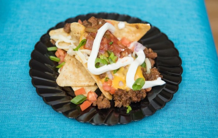 A plate of nachos topped with ground beef, cheese, sour cream, tomatoes, and green onions.