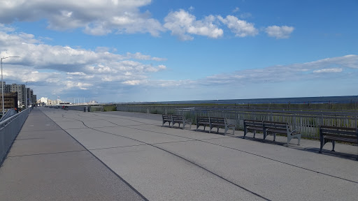 A serene coastal pathway with benches overlooking the water under a blue sky.