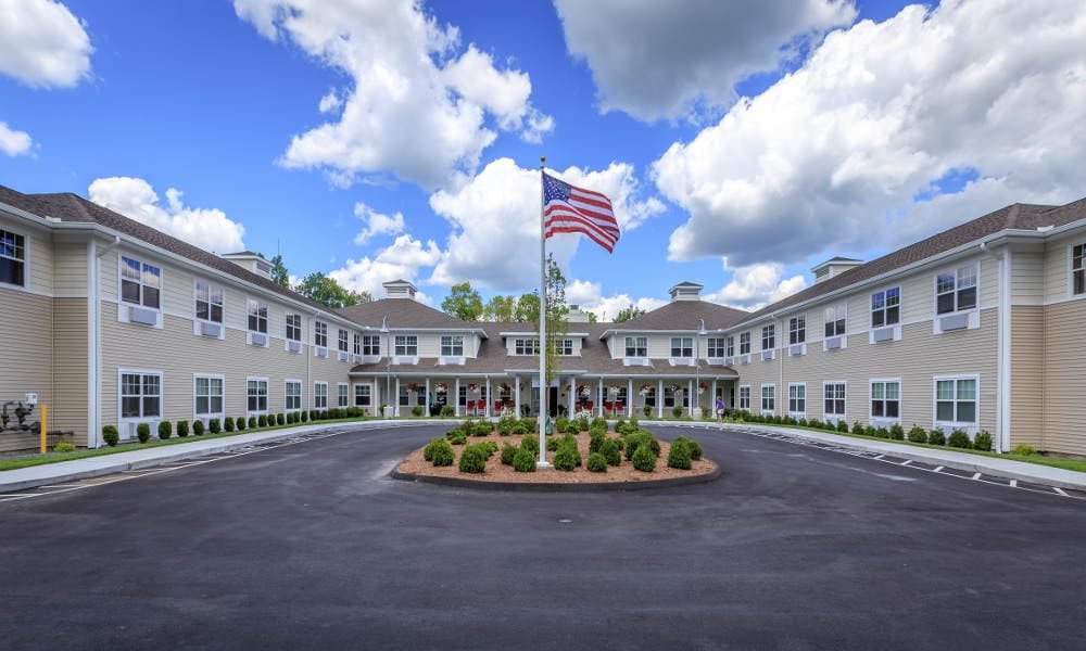 A large, symmetrical building with an American flag in front and a landscaped circular driveway under a cloudy sky.