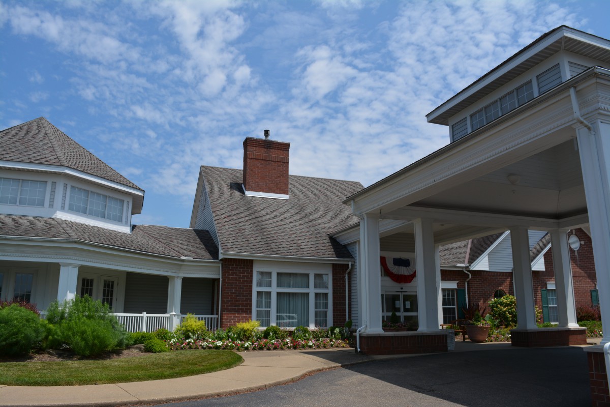 A residential building with a covered entrance and landscaped surroundings under a partly cloudy sky.