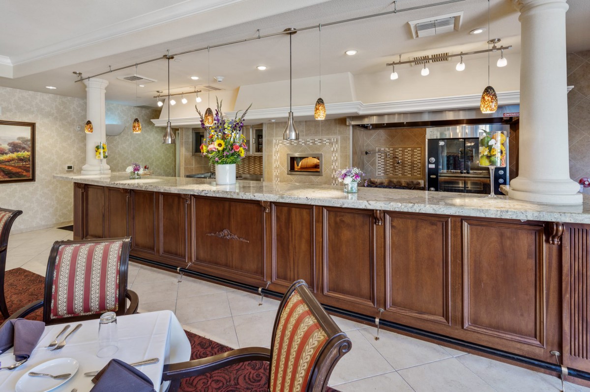 A stylish restaurant interior featuring a bar counter, seating area, and open kitchen.