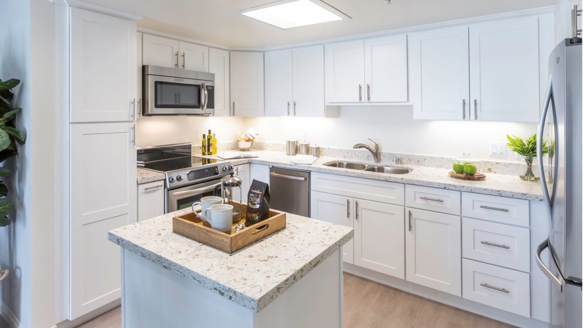 A modern kitchen featuring white cabinets, stainless steel appliances, and a central island with a marble countertop.