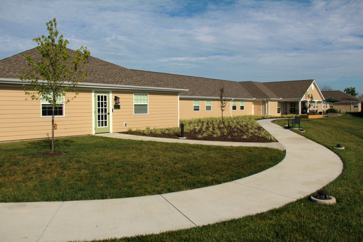 A winding pathway leads to a single-story building surrounded by well-maintained lawns.