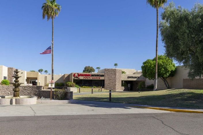 A sunny day at a hospital entrance with palm trees and an American flag.