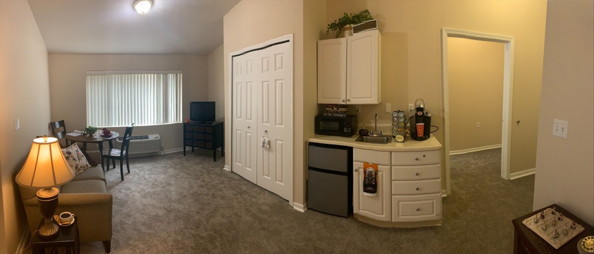 A cozy living area featuring a kitchenette with a mini fridge and storage cabinets, alongside a TV and closet.