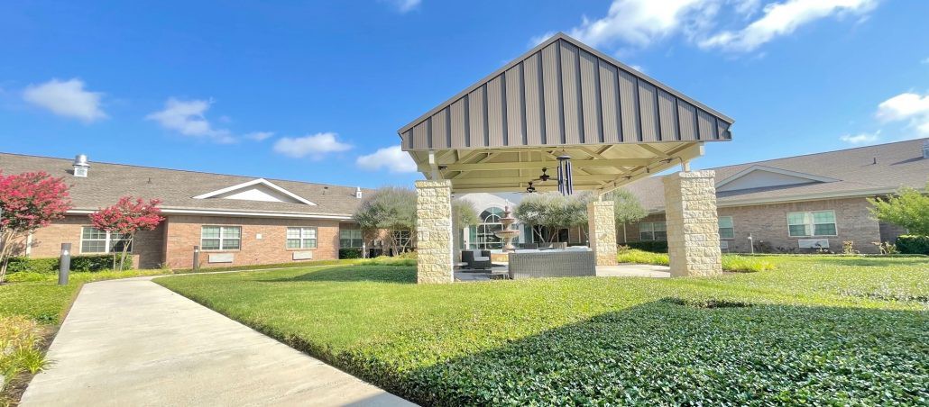 A well-maintained outdoor pavilion surrounded by a lush green lawn under a clear blue sky.