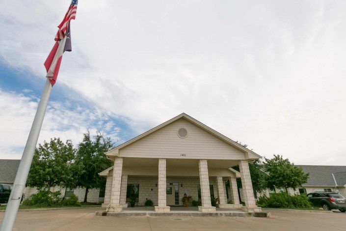 A building with columns and a flagpole against a cloudy sky.
