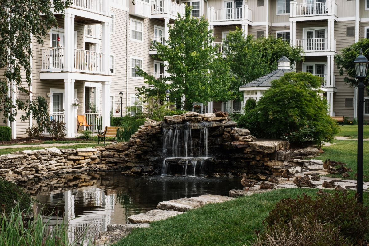 A serene waterfall and pond located in the landscaped grounds of a residential apartment complex.