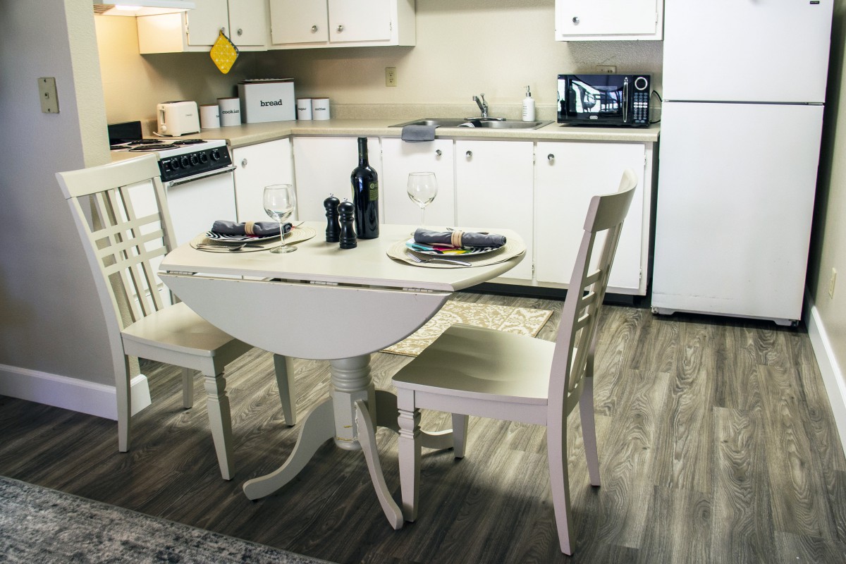 A cozy kitchen features a small dining table set for two, complete with wine and elegant place settings.