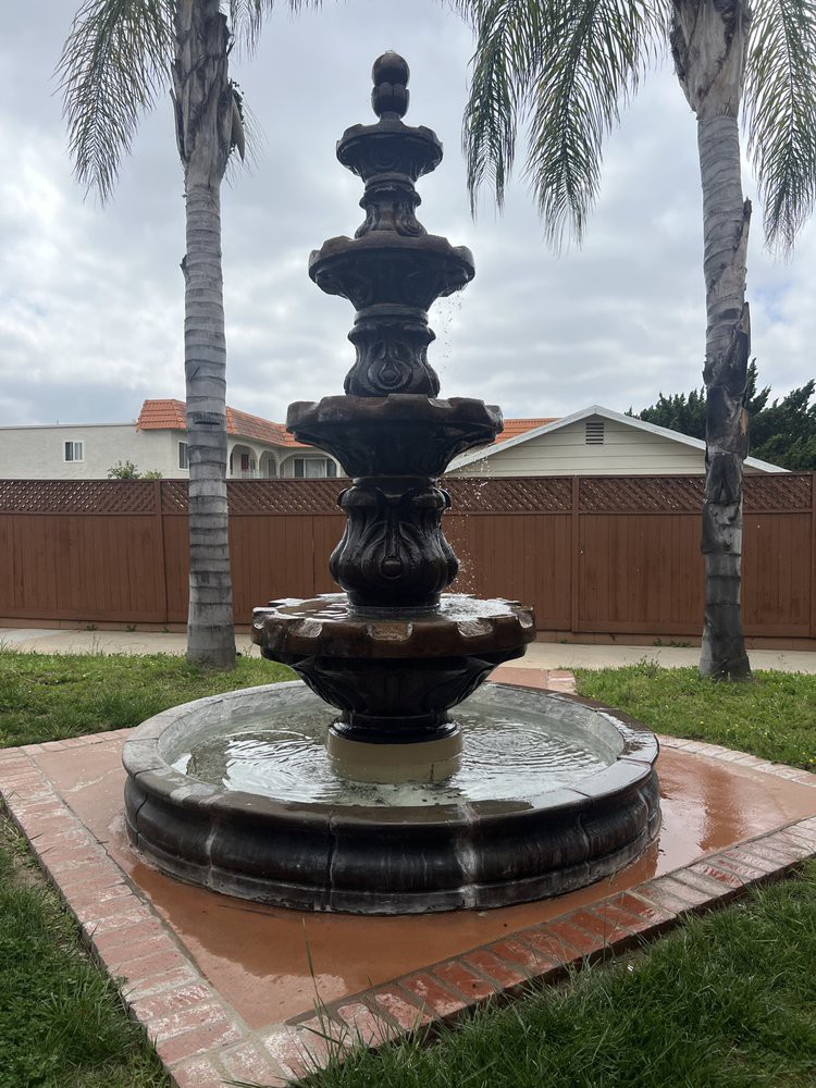 A multi-tiered fountain surrounded by palm trees in a garden setting.