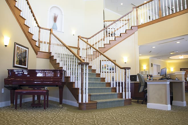 A grand staircase in a well-lit lobby, with a piano nearby and elegant interior design elements.
