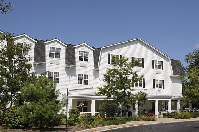 A large white residential building with surrounding greenery under a clear blue sky.