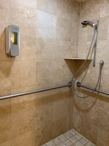A tiled bathroom shower with a grab bar, soap dispenser, and adjustable shower head.