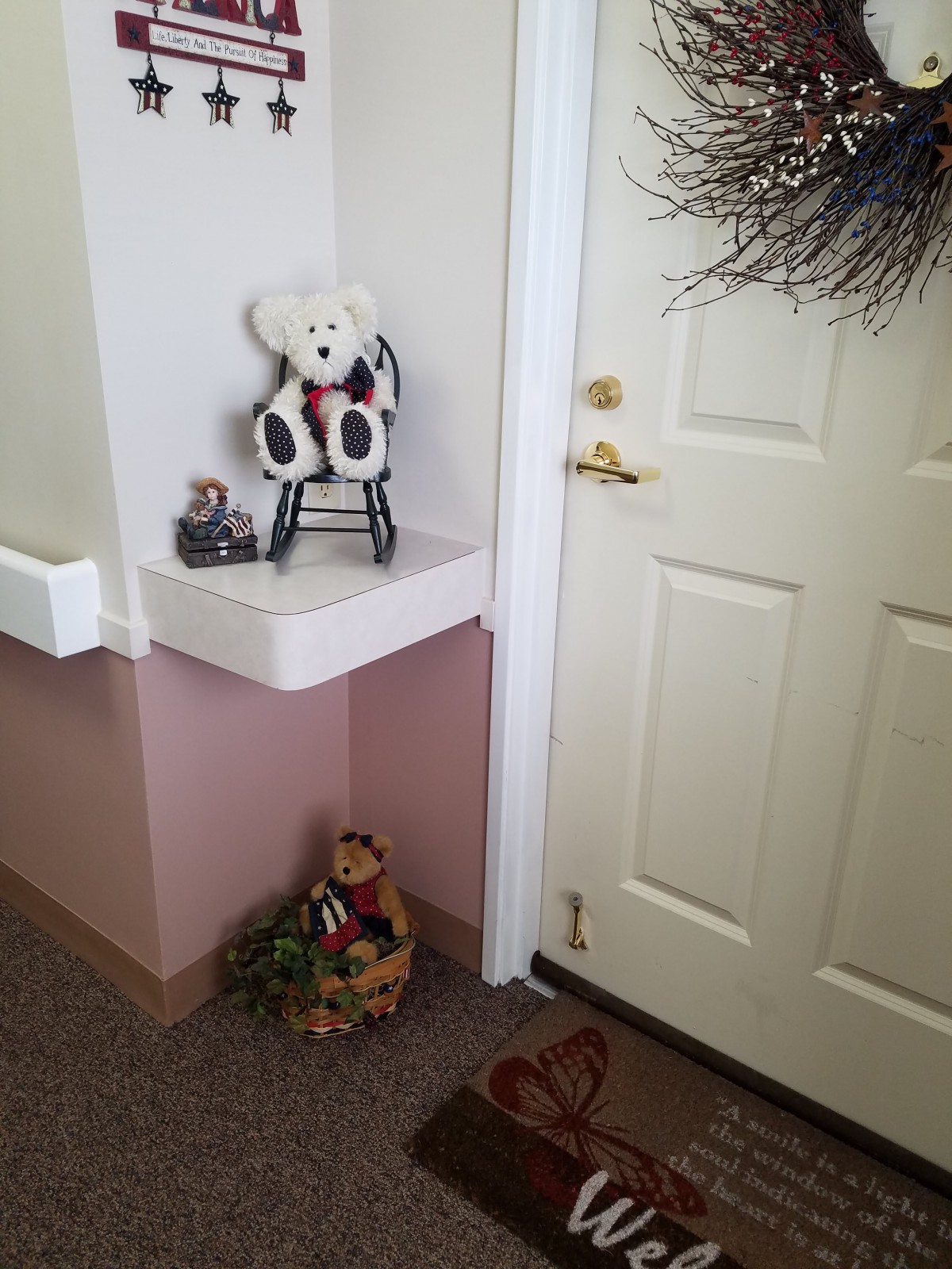 A cozy corner featuring a teddy bear on a rocking chair, a miniature car, and a basket of greenery beside a door.