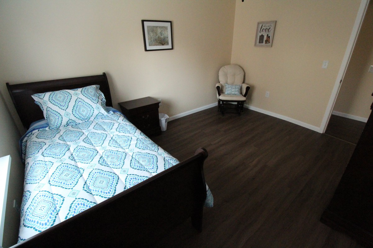 A cozy bedroom with a wooden floor, featuring a bed with patterned bedding and a comfortable chair in the corner.