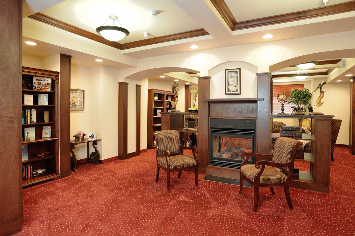 A cozy living room with a fireplace, well-furnished with chairs and a red carpet.