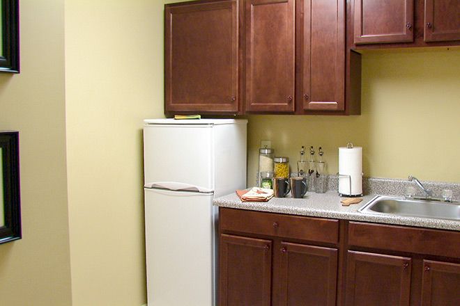 A small kitchen area featuring a white refrigerator, wooden cabinets, bottles on the countertop, and a sink.