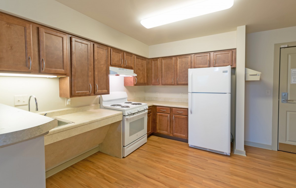 A kitchen interior featuring wooden cabinets, a white refrigerator, and an electric stove with light wood flooring.