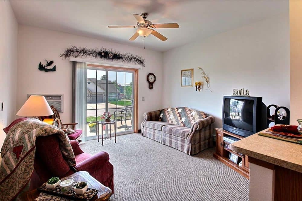 A cozy living room with a sofa, television, and ceiling fan, featuring a sliding door that opens to an outdoor view.