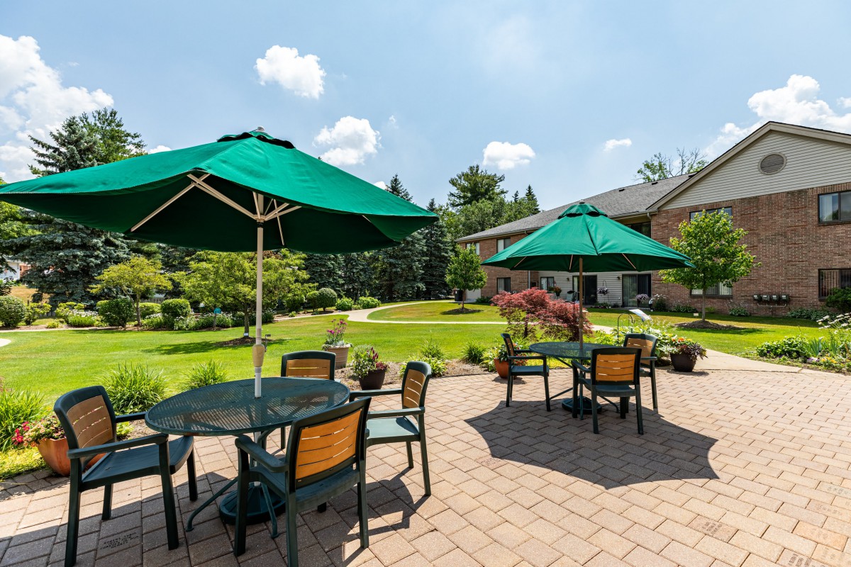 A sunny patio area with tables and green umbrellas surrounded by a lush garden.
