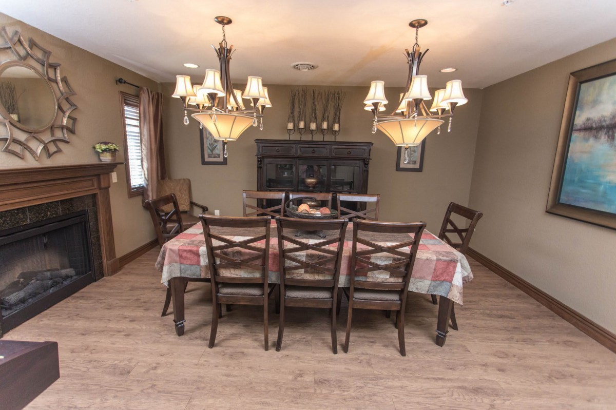 A cozy dining room with a large wooden table, surrounded by chairs and illuminated by elegant chandeliers.