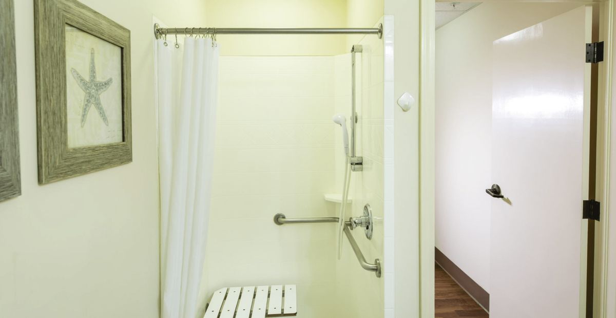 An accessible shower with a curtain, grab bars, and a foldable shower seat.